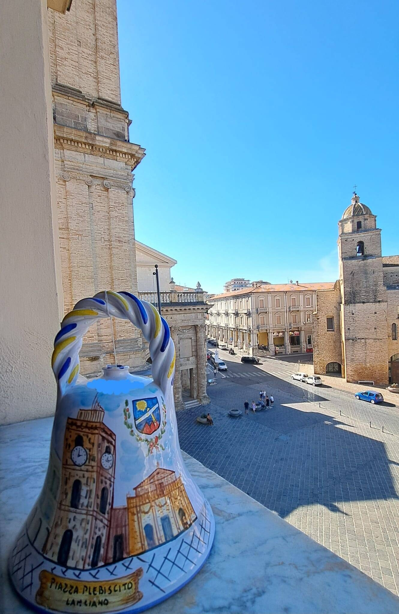 Foto di una campanella che ritrae piazza Plebiscito con la Cattedrale e la Torre Civica. Sullo sfondo, la piazza stessa.