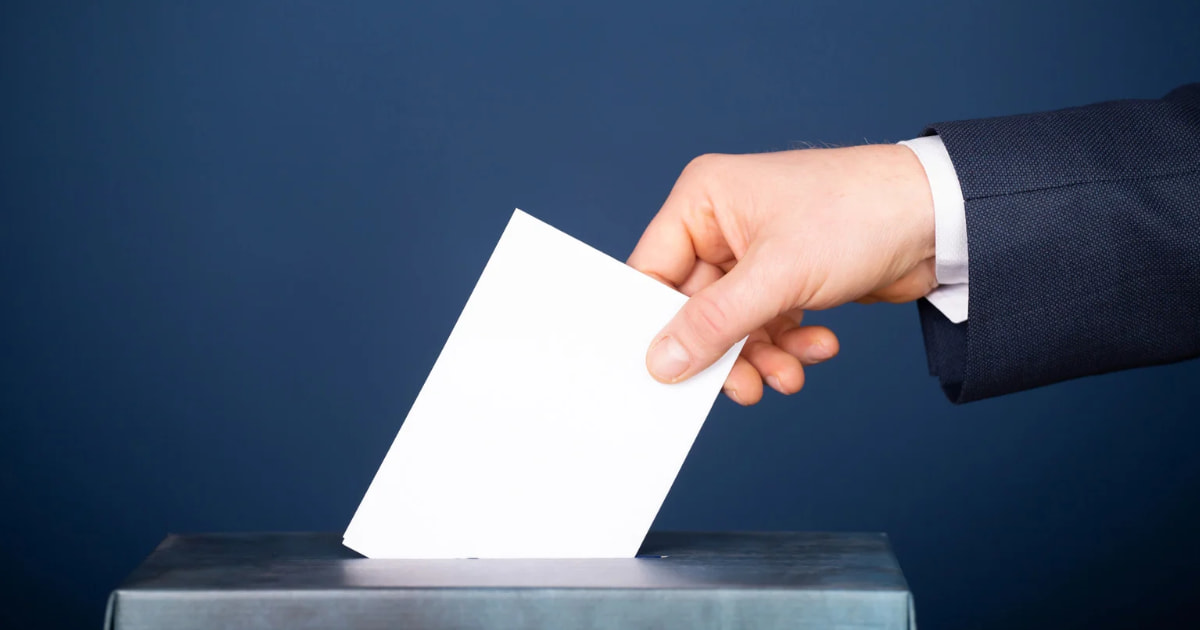 mano che tiene in mano un foglio da infilare nella scatola delle votazioni